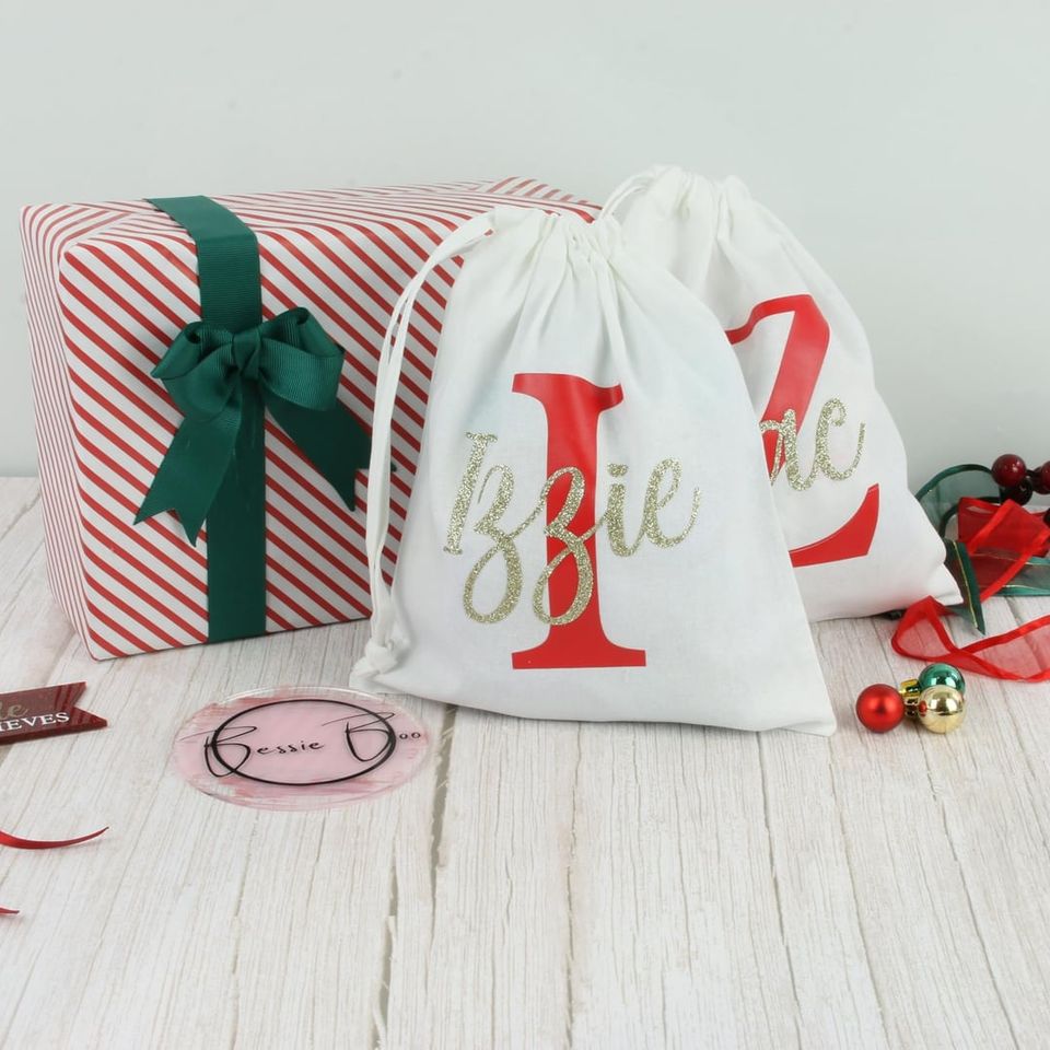 White drawstring bags with a red initial and a gold glitter name, “Izzie” and “Zac”