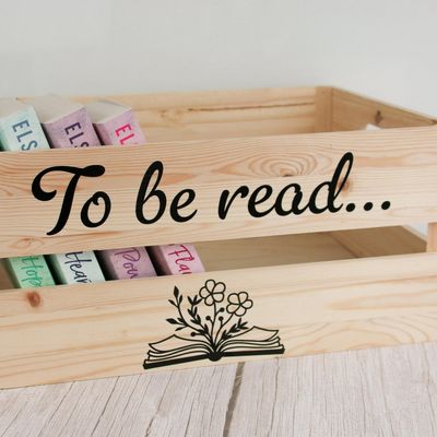 Wooden crate lettered “To be read…” with an open book and flowers, holding a row of books