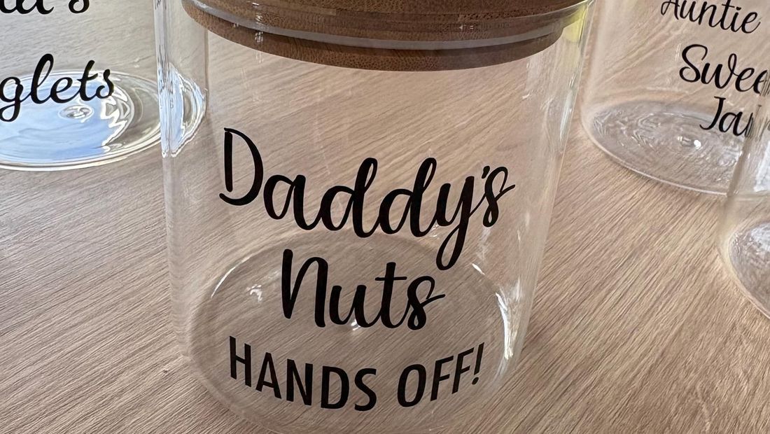 Glass jar with a bamboo lid lettered “Daddy’s Nuts, hands off!” in black vinyl